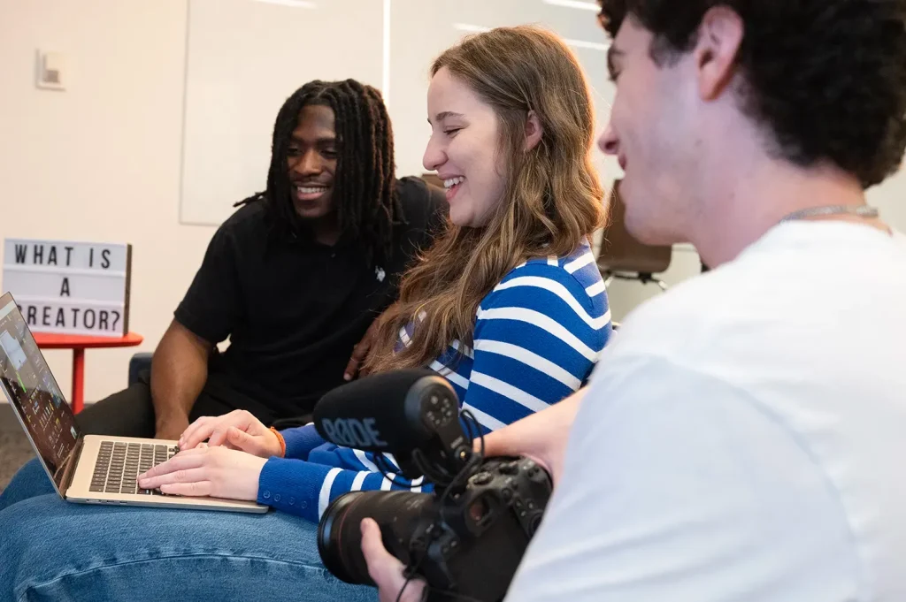 Students reviewing content on a laptop with camera equipment nearby. Photo by Matthew Nerber