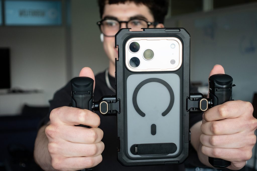 Student holding a smartphone mounted in a rig with two attached microphones for video recording